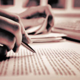 Mão segura uma caneta ao conferir texto de uma publicação científica